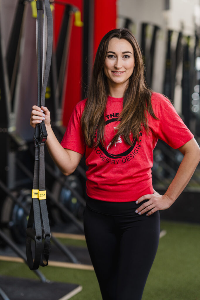The best massage therapist in Pflugerville, Rebecca Alcava, holding a TRX strap inside the Bodies By Design gym in Pflugerville.